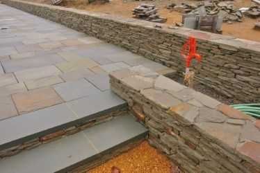 Standup fieldstone wallrock retaining wall capped with bluestone next to a flagstone patio